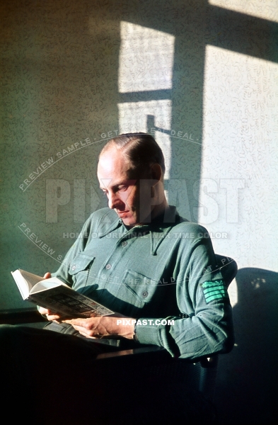 German army officer wearing green t-shirt with rank symbols on his arm and reading book. Lindau Germany 1944