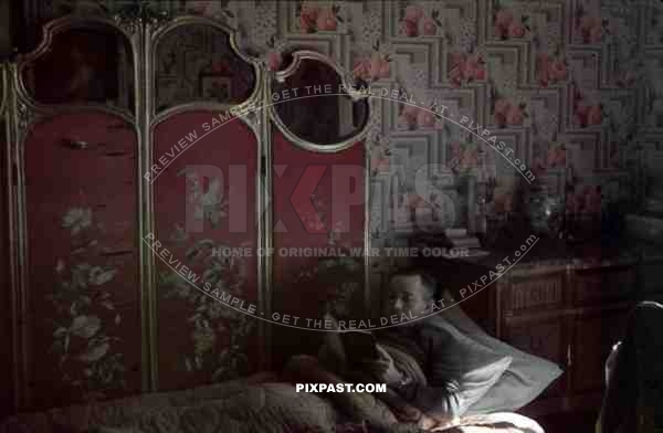 German army soldier resting in bed, French apartment, Paris 1940, reading book.