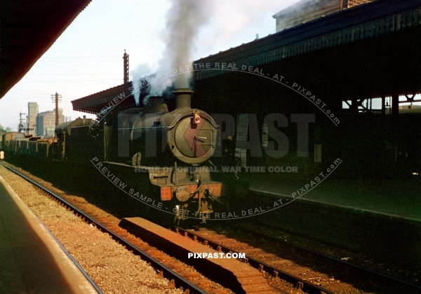 British railway steam locomotive pulling cargo into train station beside London England 1944