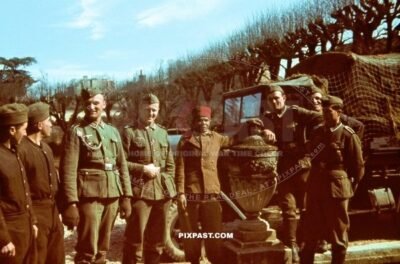 Captured French Colonial African infantry soldier with FEZ beside German army soldiers. Paris France 1940. Net truck.