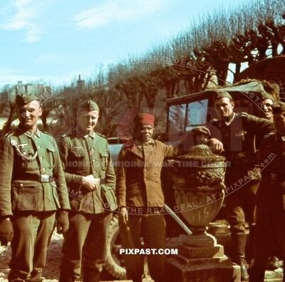 Captured French Colonial African infantry soldier with FEZ beside German army soldiers. Paris France 1940. Net truck.