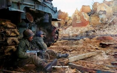 Two U.S. soldiers of C Company, 36th Armored Infantry Regiment, 3rd Armored Division shelter behind M-4 Sherman