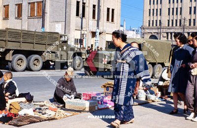 Japanese women with baby on back inspect soldier veteran soldier selling american products on street in Tokyo Japan 1945